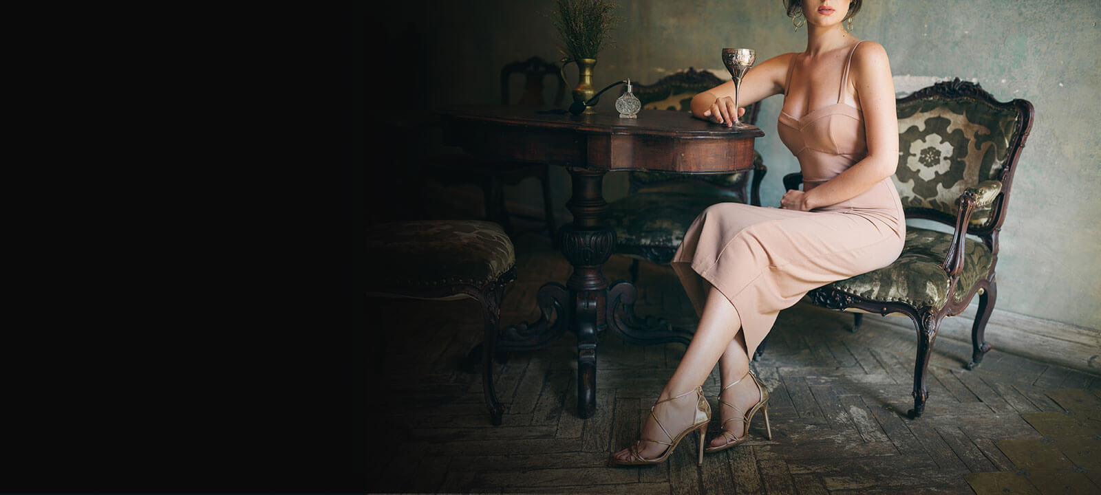 Woman in cocktail dress sitting at a table, drinking wine from a gold cup